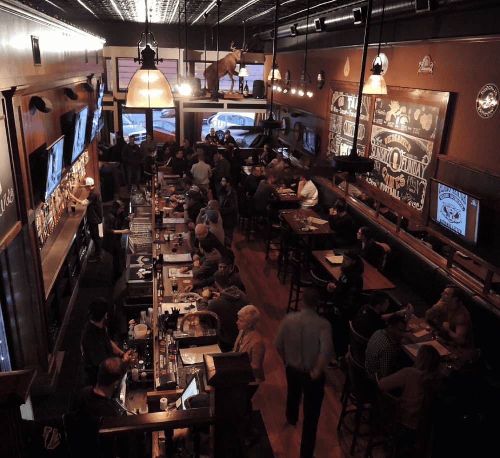 Cozy sports bar interior with patrons watching games, bar staff, and sports memorabilia, offering a vibrant atmosphere for sports fans.