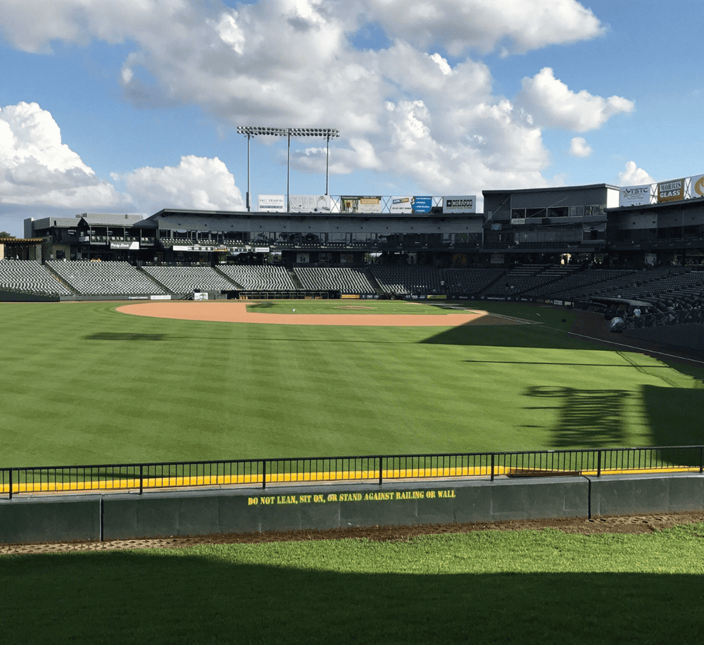 Bright baseball stadium with green field and seating, under a partly cloudy sky, ideal for sports event directions.