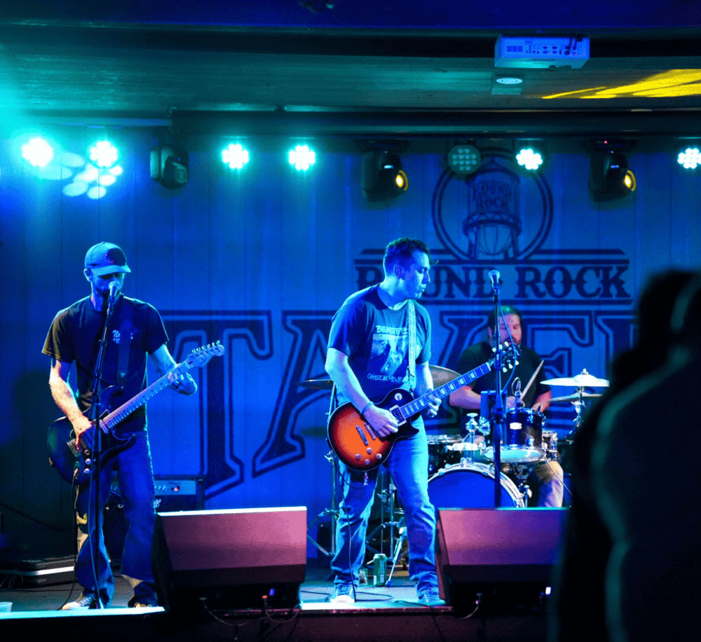 Energetic live band performing on stage at a rock concert with colorful lights and audience engagement.
