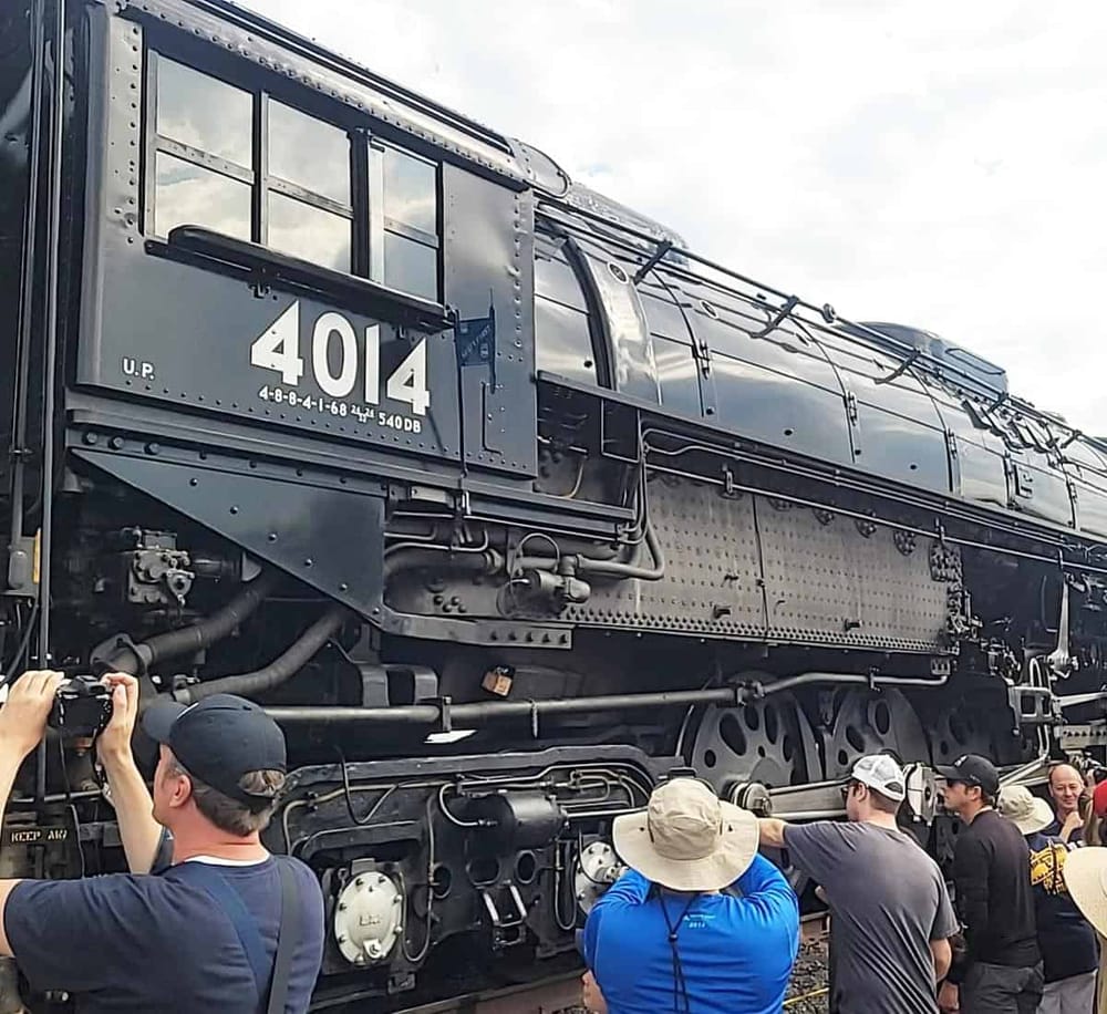 Vintage steam locomotive with tourists viewing and taking photos, historical train experience, railroad adventure, museum or heritage site.