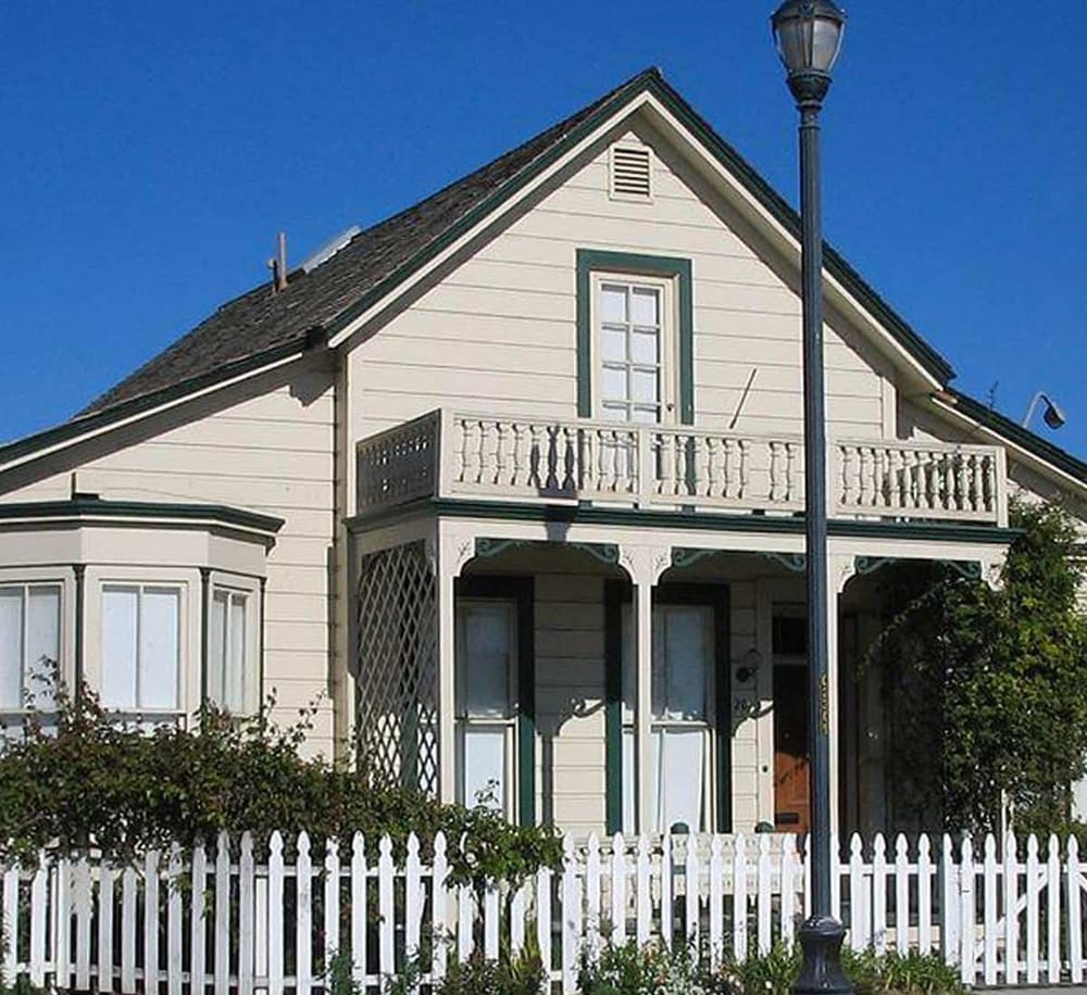 Charming Victorian house with white exterior, decorative balcony, and picket fence.