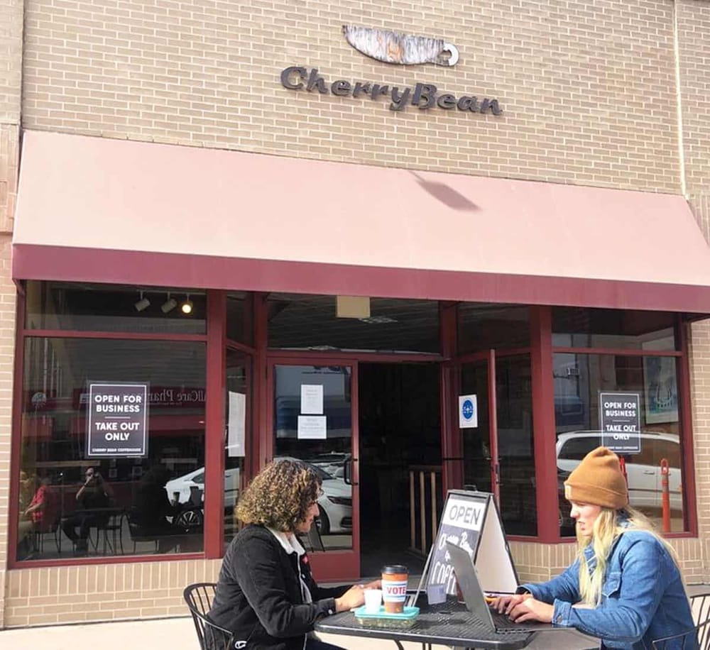 Outdoor dining at Cherry Bean coffee shop with customers working on laptops, storefront signage visible.