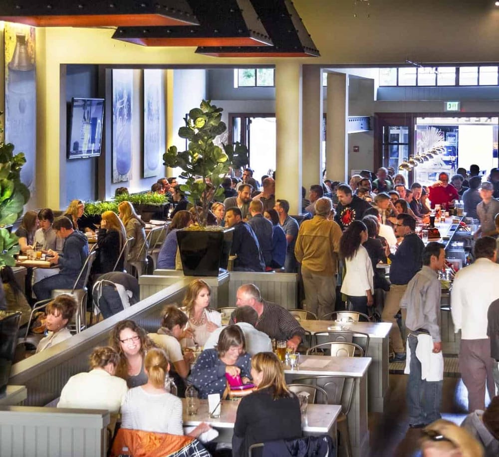 Busy restaurant interior filled with diverse group of people enjoying meals and drinks while socializing.