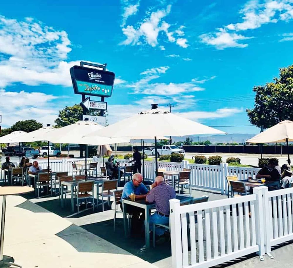Outdoor dining at Quest for Directions restaurant with umbrellas and happy patrons.
