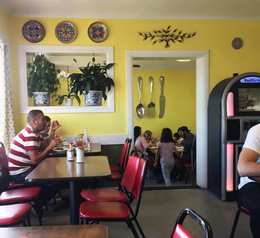 Colorful interior of a restaurant with diners enjoying their meals, featuring yellow walls, decorative plates, and a jukebox.