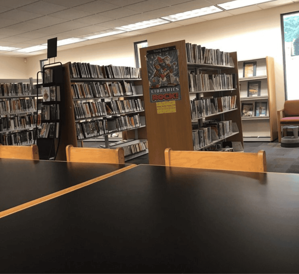 Aisle of bookshelves in a library, with a 'Libraries Rock!' sign in the center.