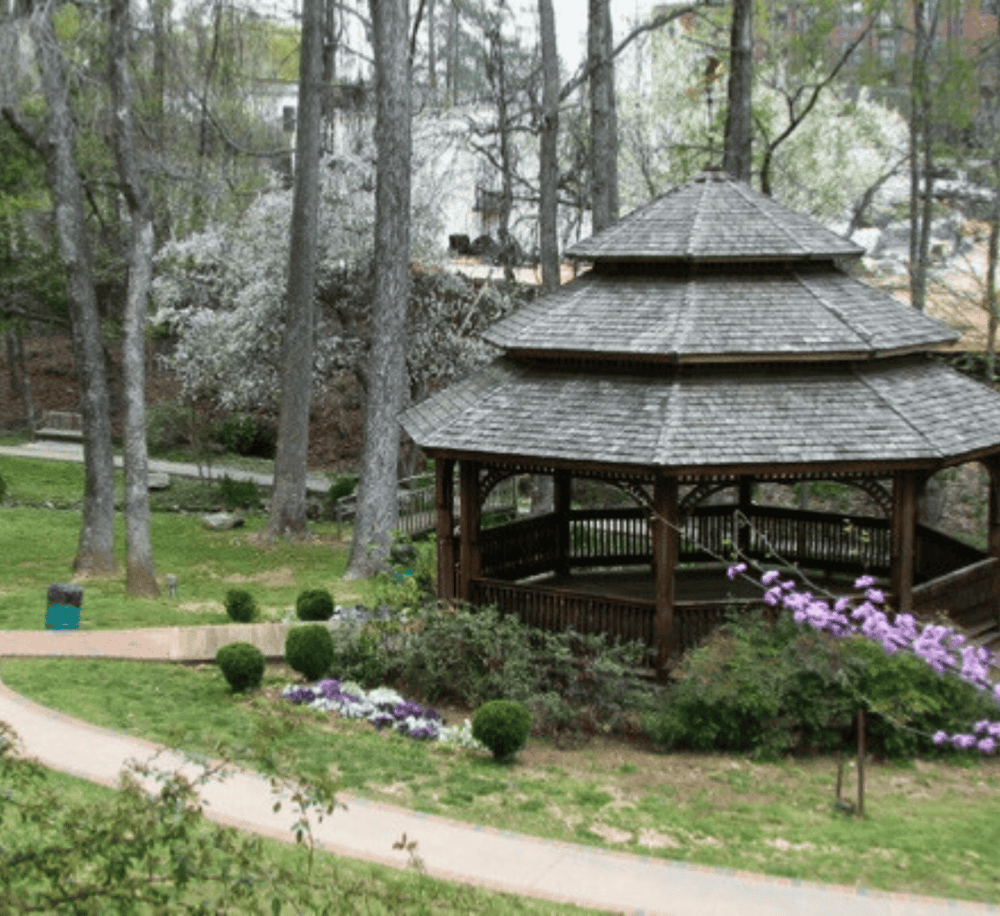 Serene outdoor park with wooden gazebo surrounded by trees and colorful flowers, ideal for relaxation and nature walks.