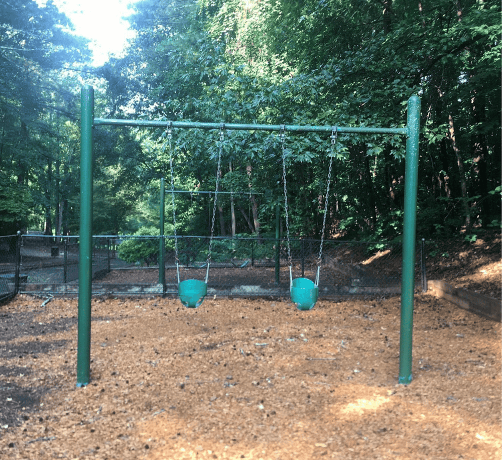 Bright green playground swings in a lush wooded park setting.