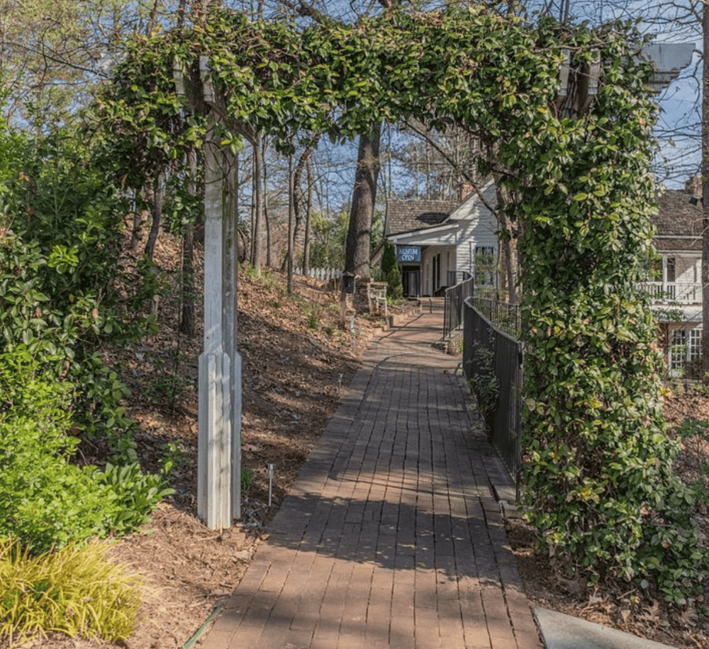 Welcoming garden archway leading to historic downtown, scenic brick pathway, lush landscaping, and charming neighborhood.