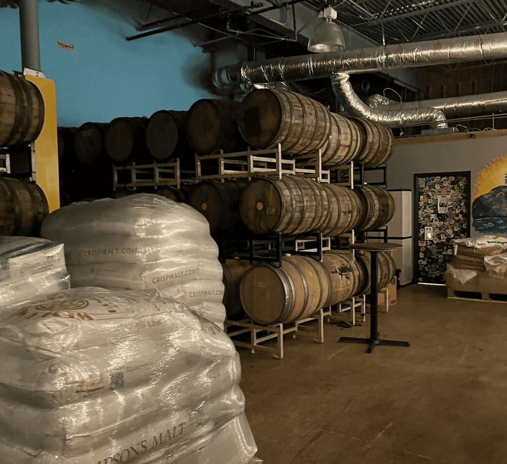 Barrels and malt bags in a craft distillery storage area.