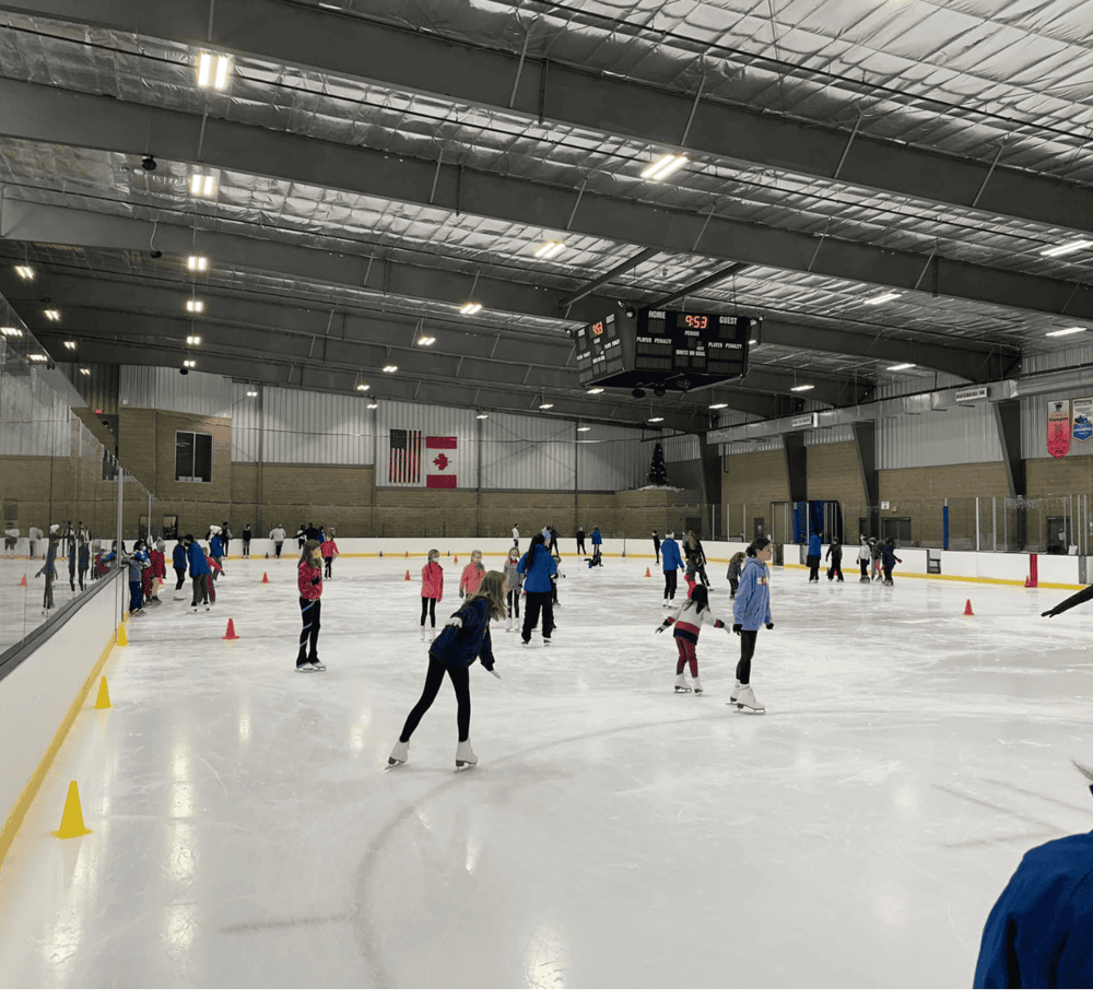 Ice skating rink with people enjoying skating, indoor sports facility, and a high ceiling.