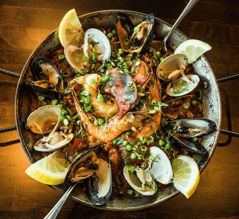 Steamed seafood paella with shrimp, mussels, and lemon wedges in a rustic pan. Authentic Spanish seafood dish.