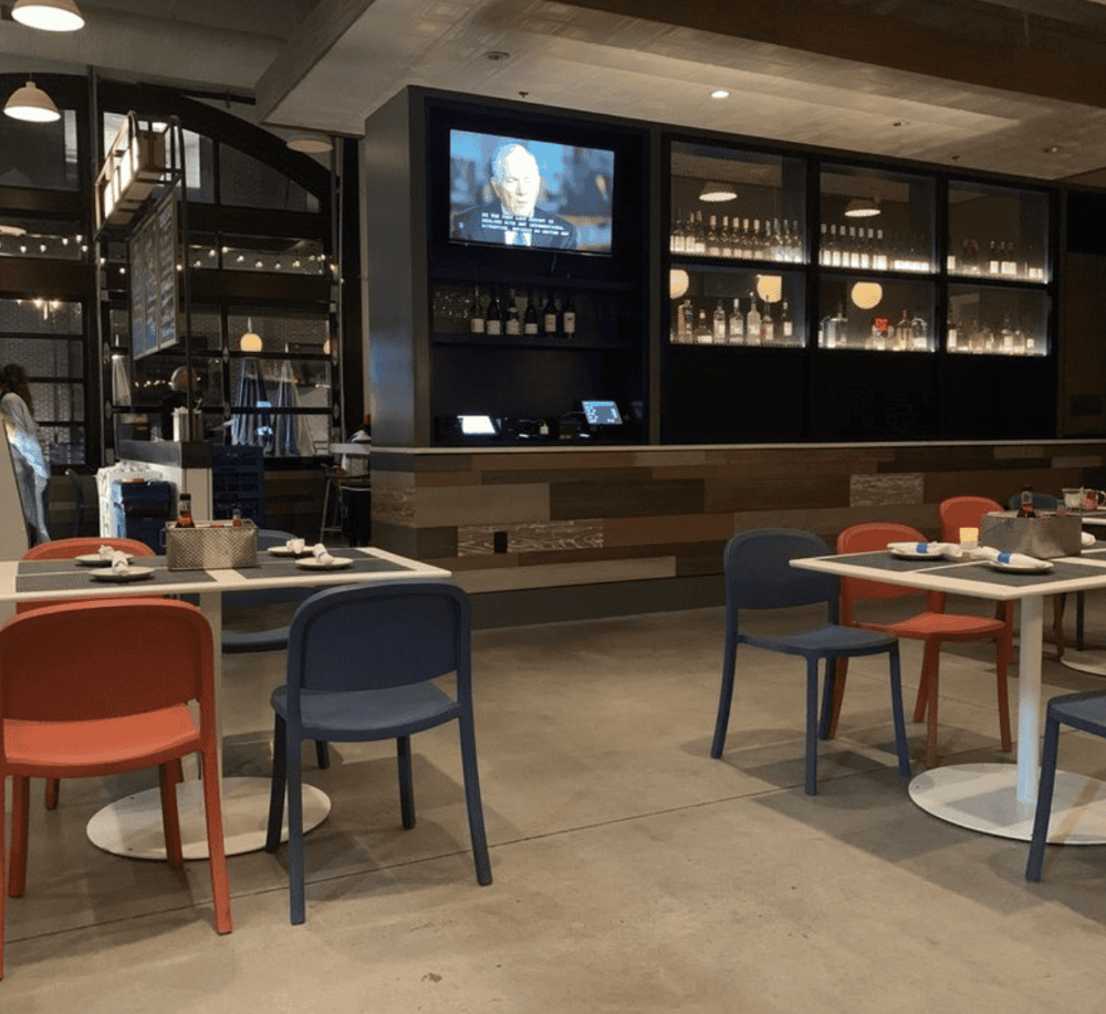 Cozy restaurant with modern decor, colorful chairs, and a large screen TV, perfect for dining and socializing.