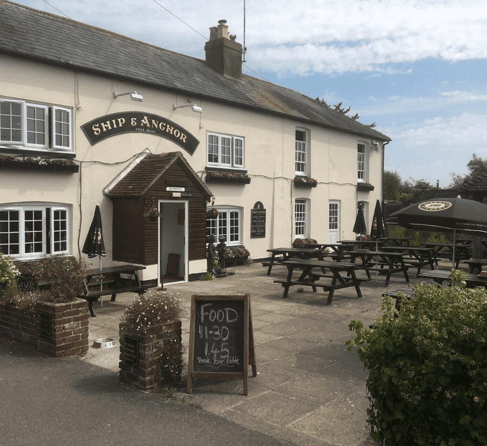 Cozy country pub with outdoor seating, garden planters, and welcoming atmosphere, ideal for dining and relaxation.
