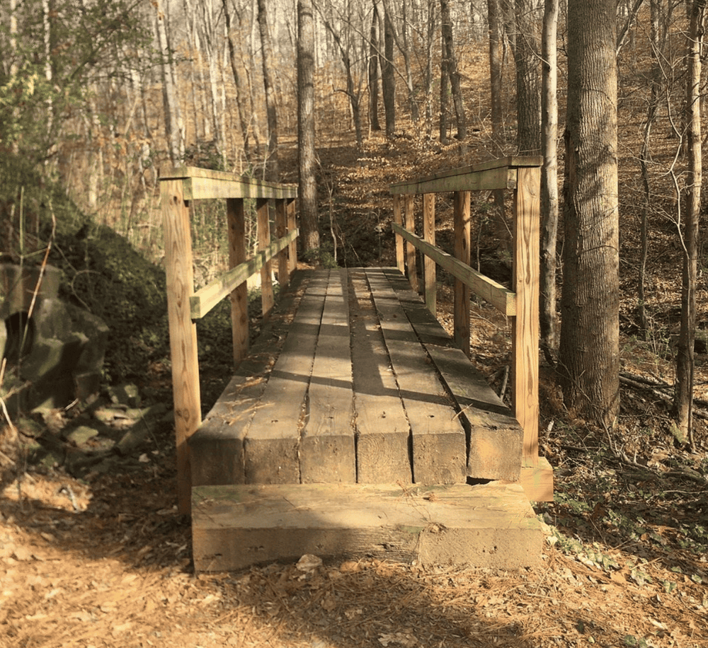 Wooden nature trail bridge in forestExplore scenic hiking trails with QuestForDirections' outdoor navigation solutionsImage of a handcrafted wooden bridge in the woods, showcasing outdoor navigation and nature exploration using QuestForDirections.