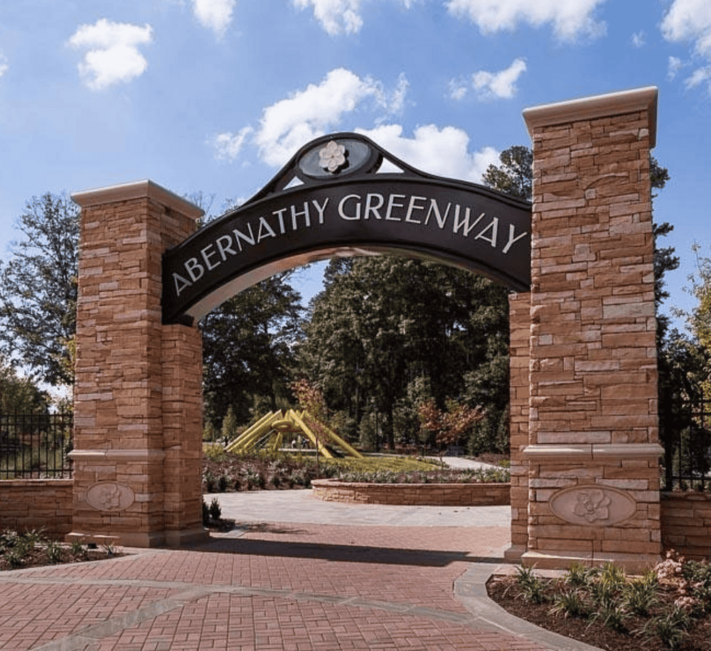 Welcoming entrance of Abernathy Greenway park with brick archway and lush greenery in the background.
