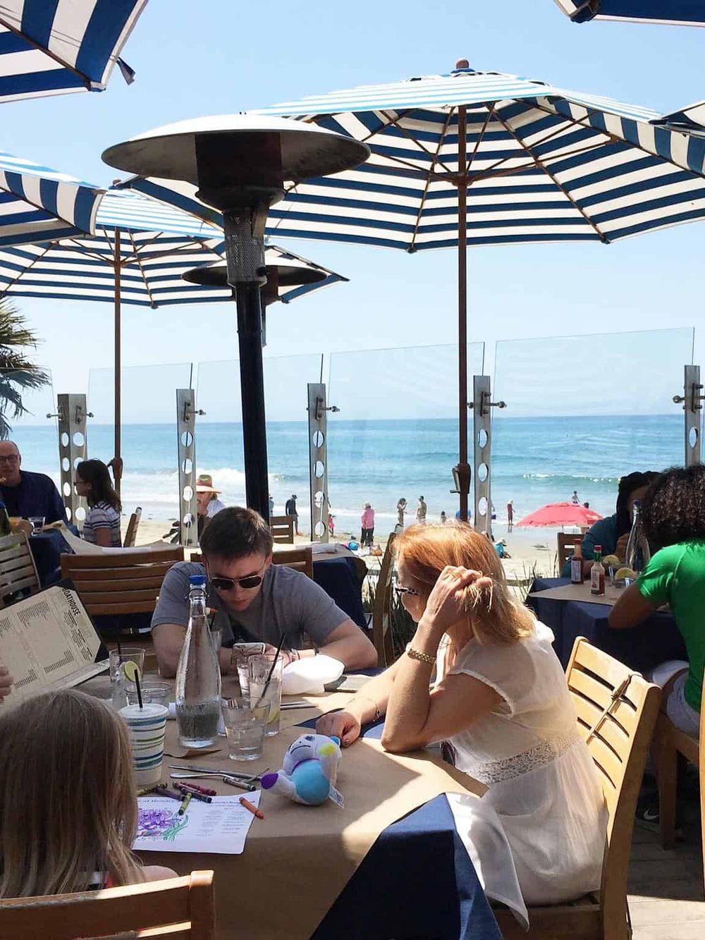 Beachside restaurant with umbrellas and ocean view, people dining and relaxing by the sea.
