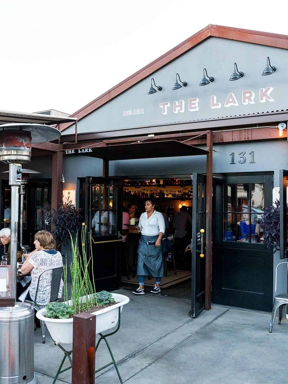 Outdoor dining at The Lark restaurant with a welcoming entrance and patrons enjoying their meals.