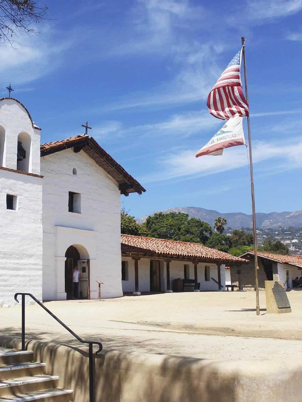Historic mission church architecture in California with American flags and scenic mountain views.