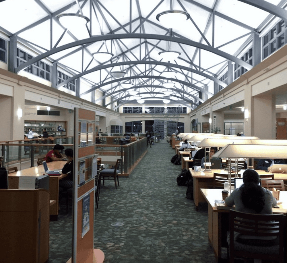 Bright indoor library with high glass ceiling, modern lighting, and study tables, perfect for research and reading.