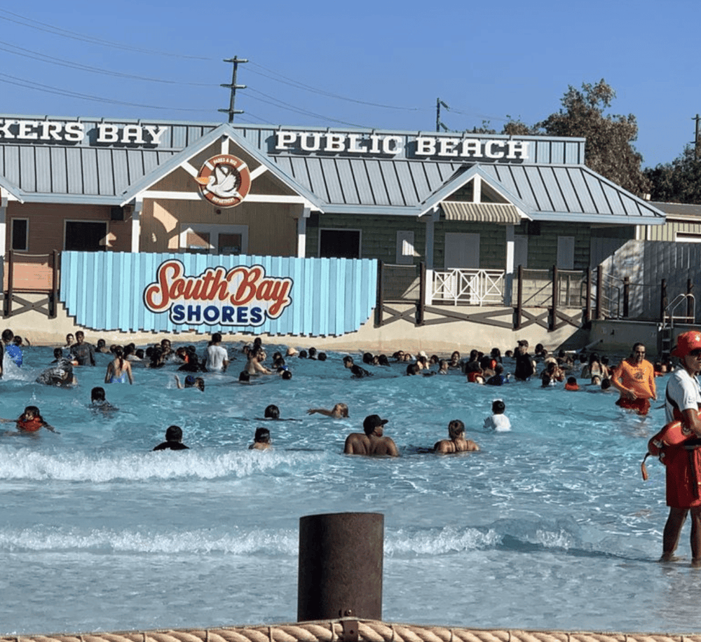 Brightly lit South Bay Shores water park with many visitors swimming and enjoying the beach scene.