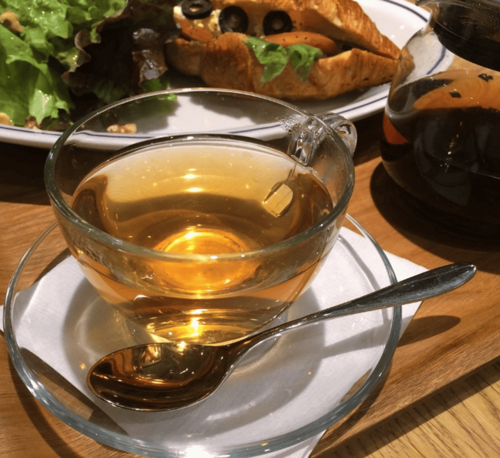 Hot tea served in a glass cup with a spoon on a wooden table.
