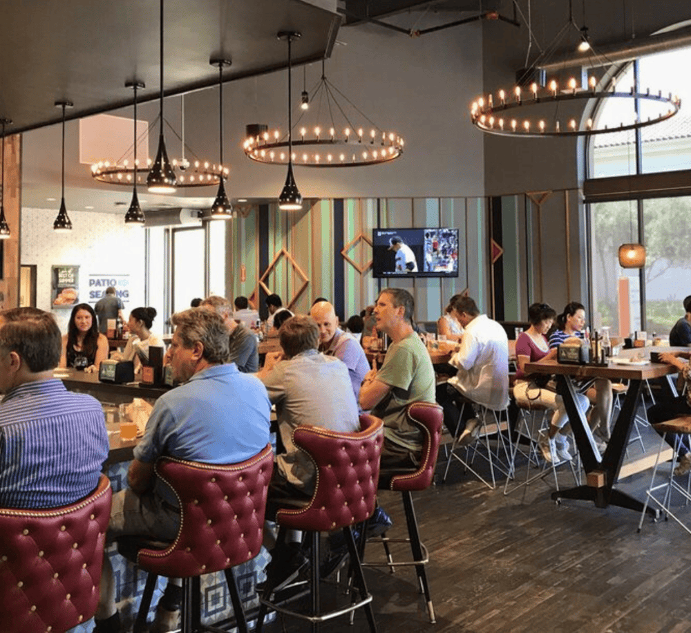 Modern restaurant interior with diverse diners, stylish lighting, and large windows for a welcoming dining experience.