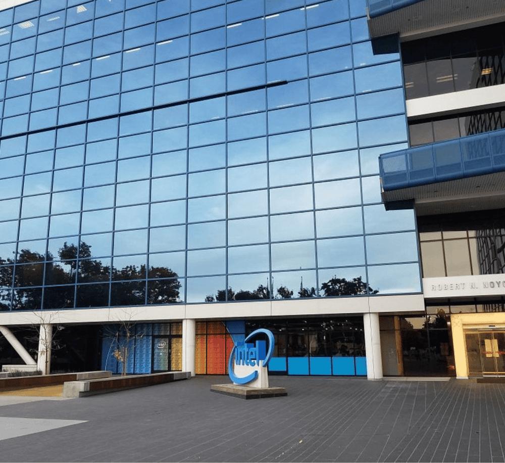 Modern corporate office building with reflective glass exterior, QuestForDirections logo in front, and outdoor plaza.