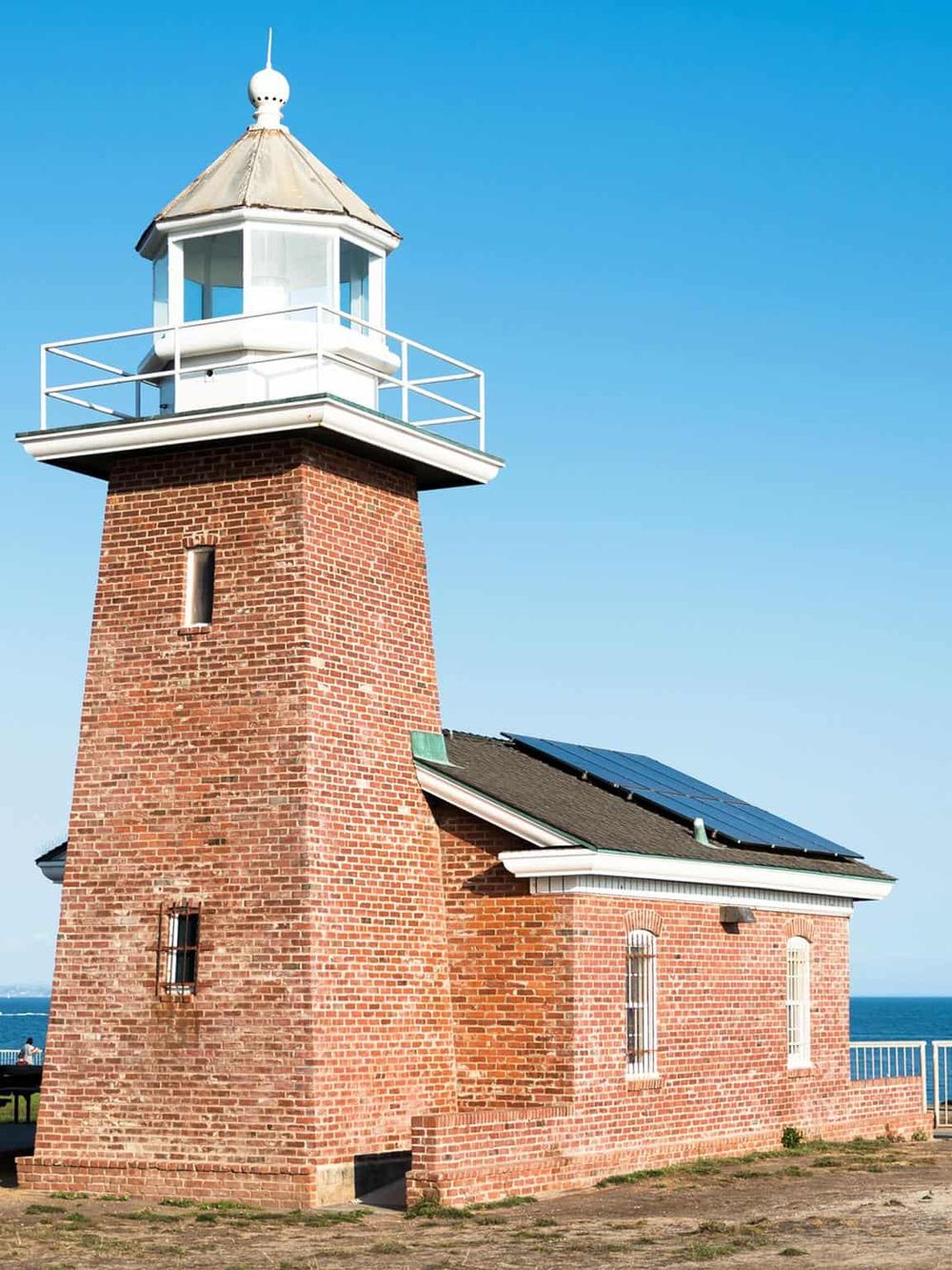 Lighthouse by the ocean with solar panels, during clear weather, representing navigation and travel assistance.