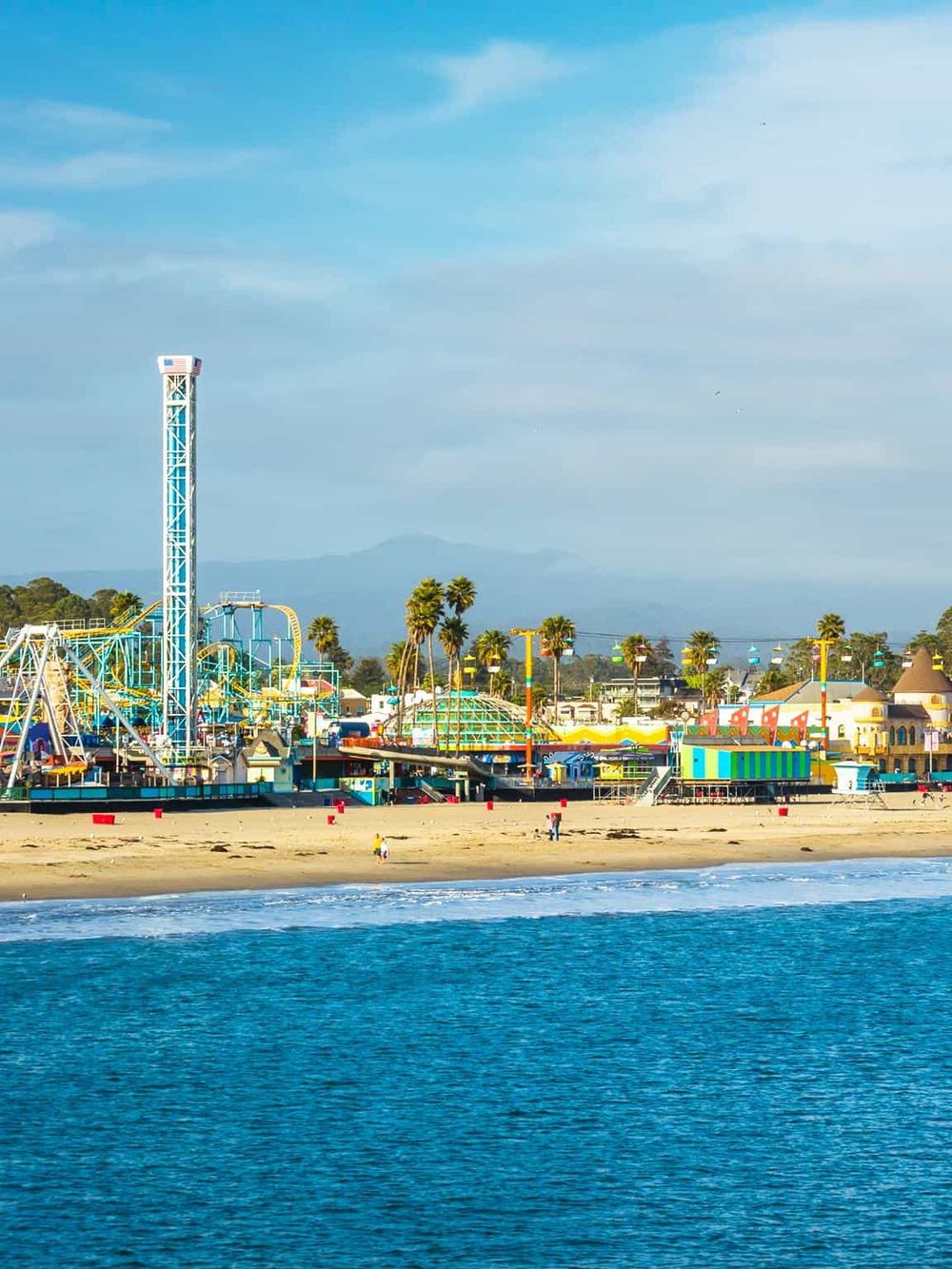Colorful amusement park at the beach with rides and palm trees, ideal for family fun and seaside entertainment.
