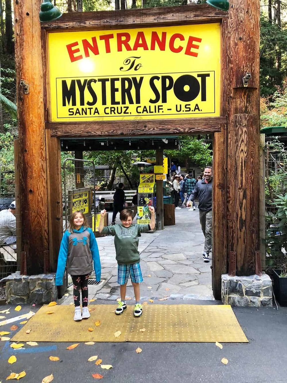 Colorful entrance sign to Mystery Spot Santa Cruz, California, with visitors excited to explore.