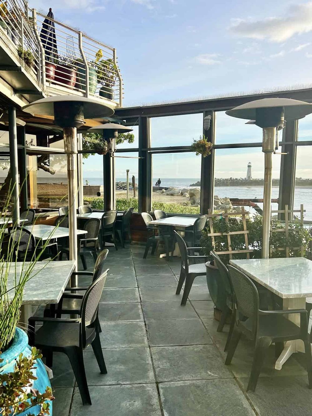 Outdoor dining area with ocean view and lighthouse in the background. Perfect for a relaxing seaside restaurant experience.
