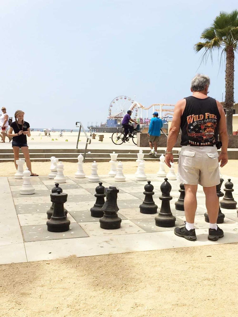 Large outdoor chess game on beach promenade with Ferris wheel in background - ideal for coastal recreation and outdoor activities.