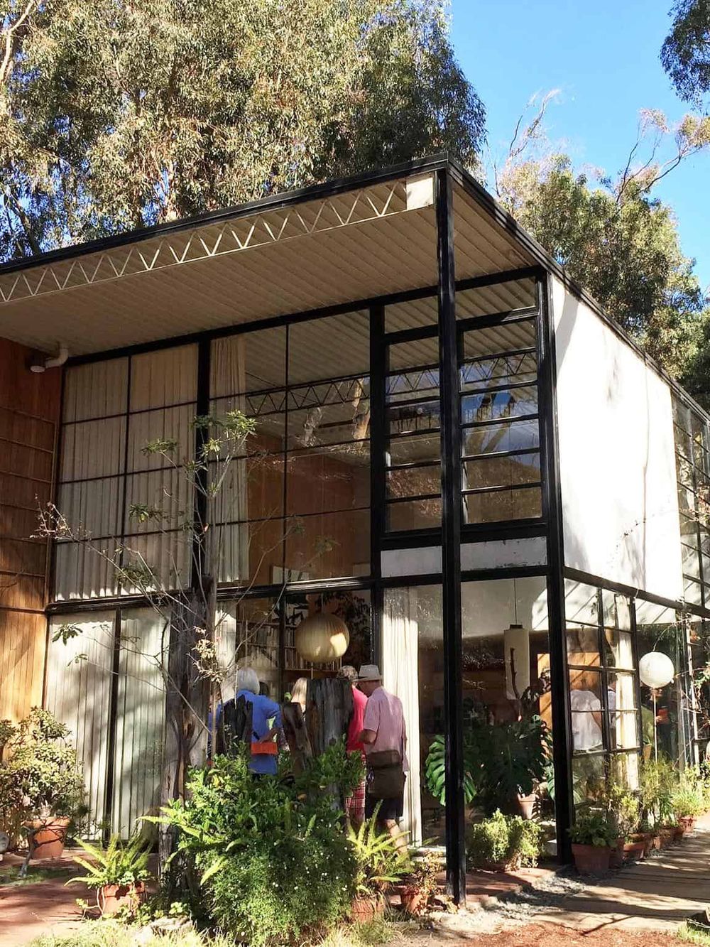 Colorful modern building with glass walls, outdoor plants, and clear blue sky.