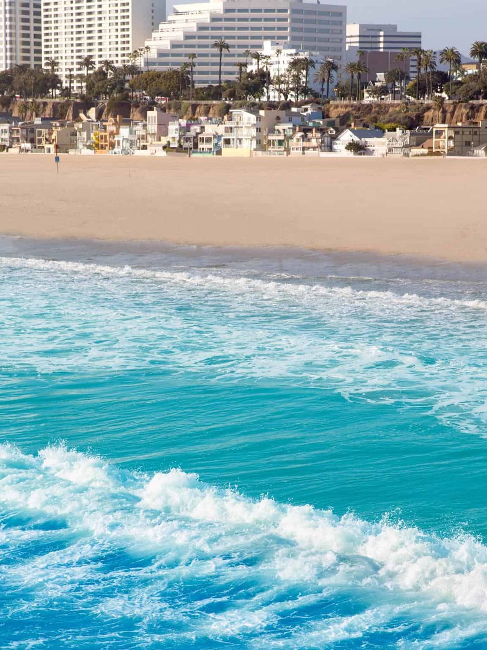 Vibrant beach scene with ocean waves and a cityscape with high-rise buildings in the background.