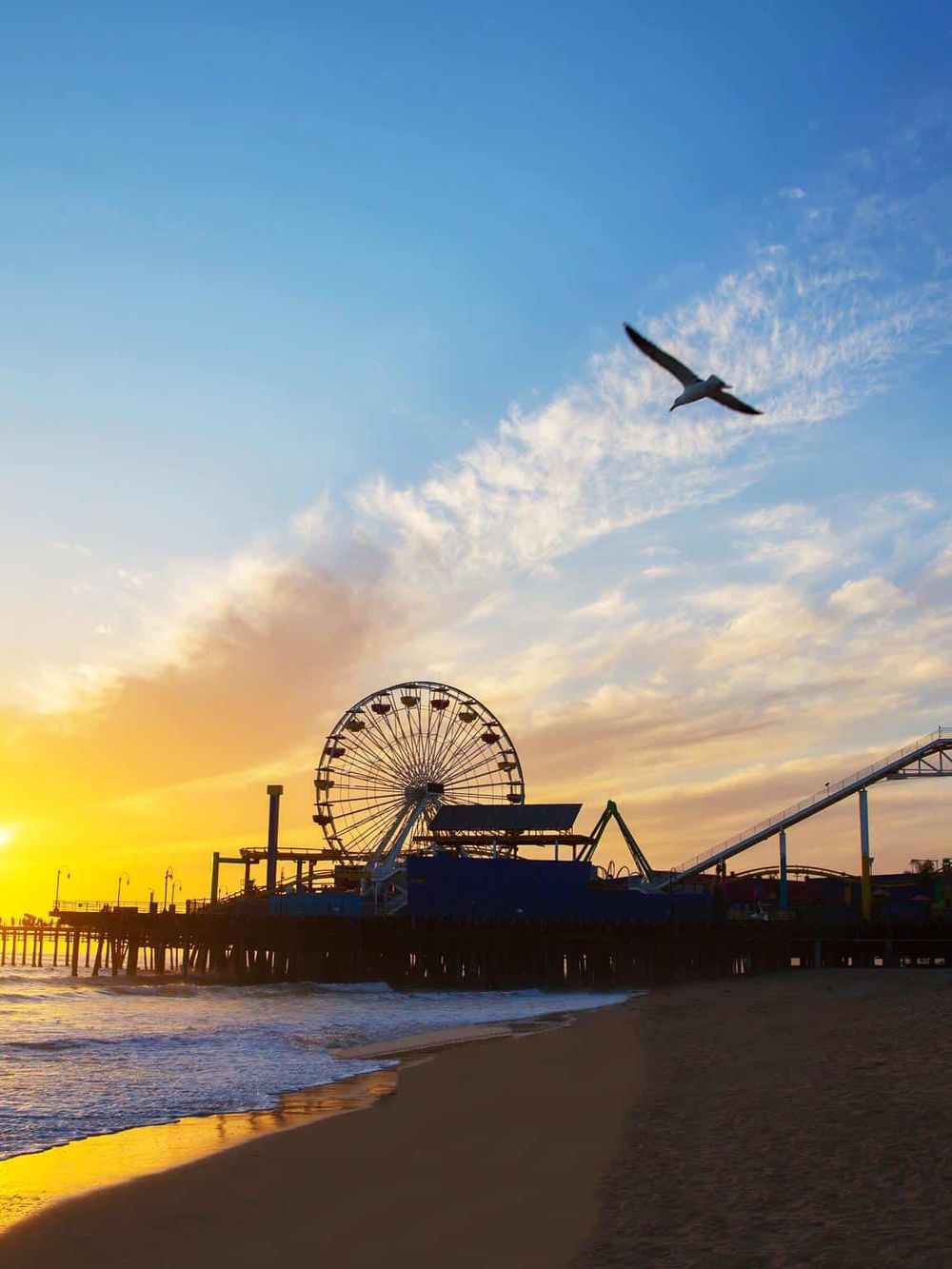 Colorful sunset at Pacific Park Pier with Ferris wheel and roller coaster on Santa Monica Beach, California.