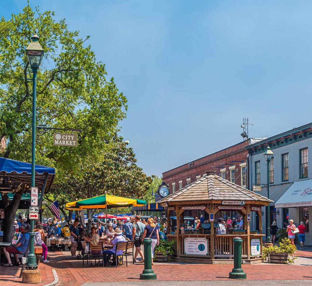 Colorful city market with outdoor seating, vibrant umbrellas, and bustling shoppers on a sunny day.