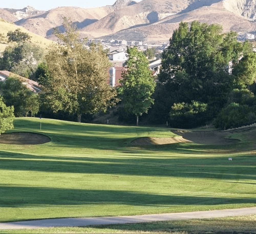 Lush golf course with rolling greens, trees, and mountain views in the background.