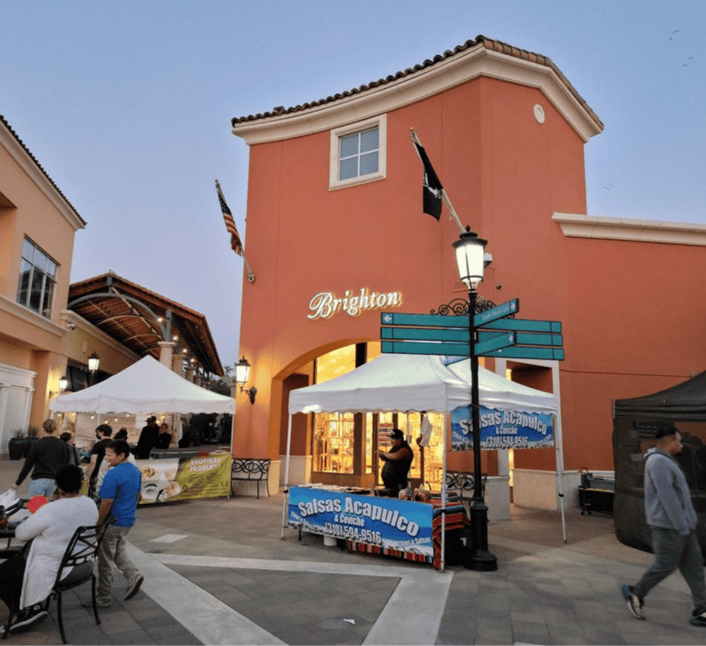 Brighton shopping center in California with outdoor market and flags, at dusk.
