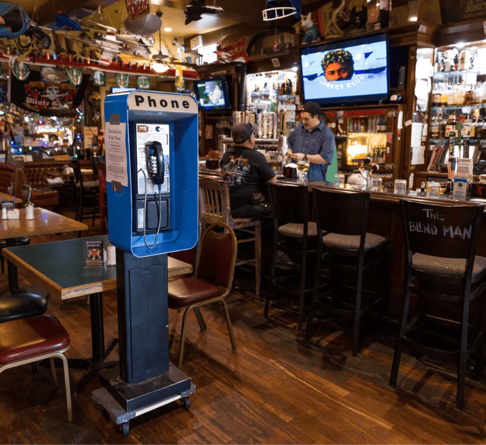 Phone booth at a cozy bar with patrons and television screens, ideal for local nightlife and dining experiences.