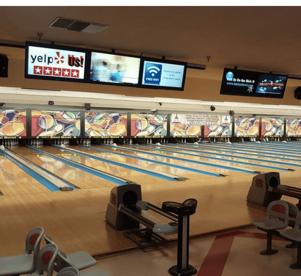Bright bowling alley with multiple lanes and digital screens showing advertisements and reviews.
