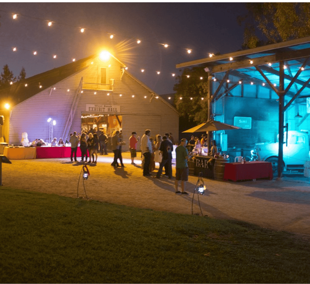 Bright outdoor event at Quest for Directions venue with string lights and a barn-style exhibit hall, perfect for community gatherings.