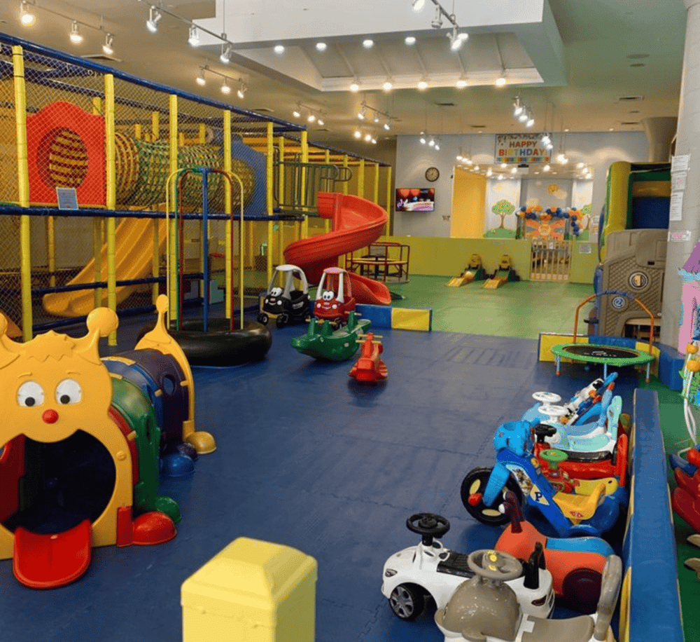 Colorful indoor kids' play area with slides, ride-on toys, and soft play zones.