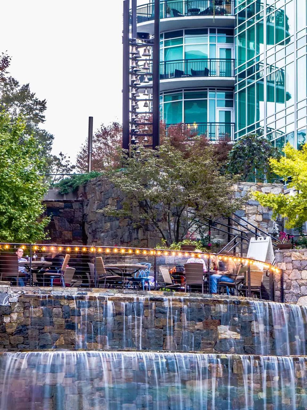 Modern urban building with outdoor dining area and waterfall feature, showcasing innovative architecture and scenic views.