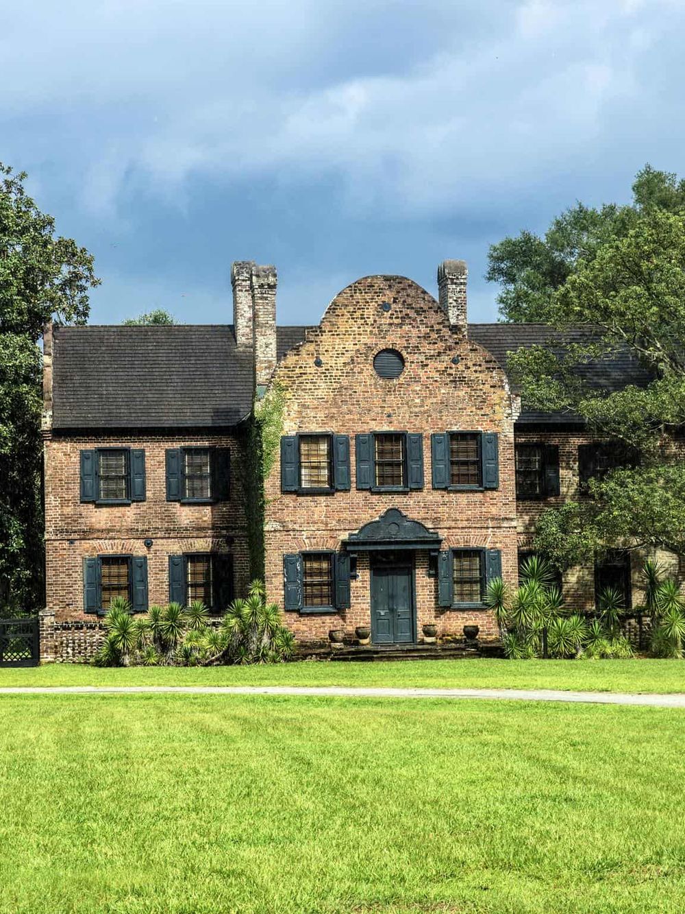 Historic brick house with dark shutters and lush greenery, ideal for exploring homestead tours.