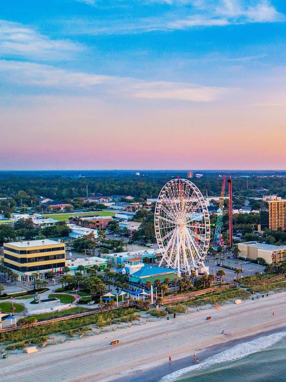 Amusement park overlooking the beach with a large Ferris wheel and skyline at sunset, ideal for travel and tourism SEO.