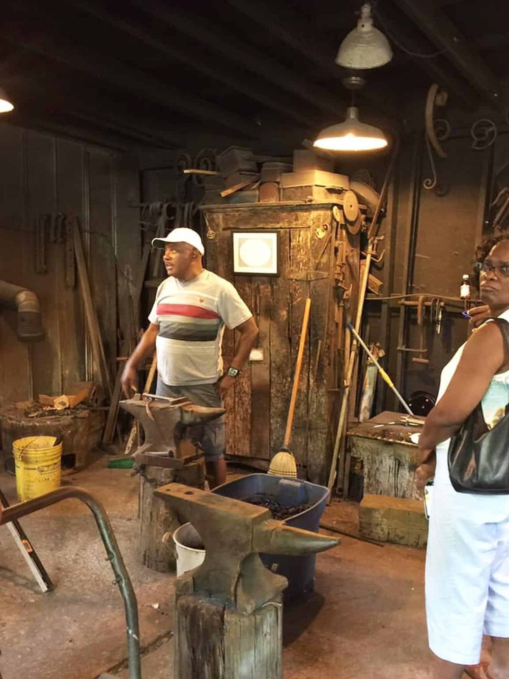 Blacksmith forging metal tools in a rustic workshop with antique equipment and wooden surroundings.