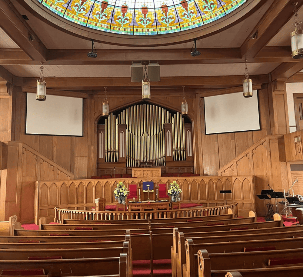 Elegant church sanctuary with wooden interior, stained glass dome, and organ pipes.