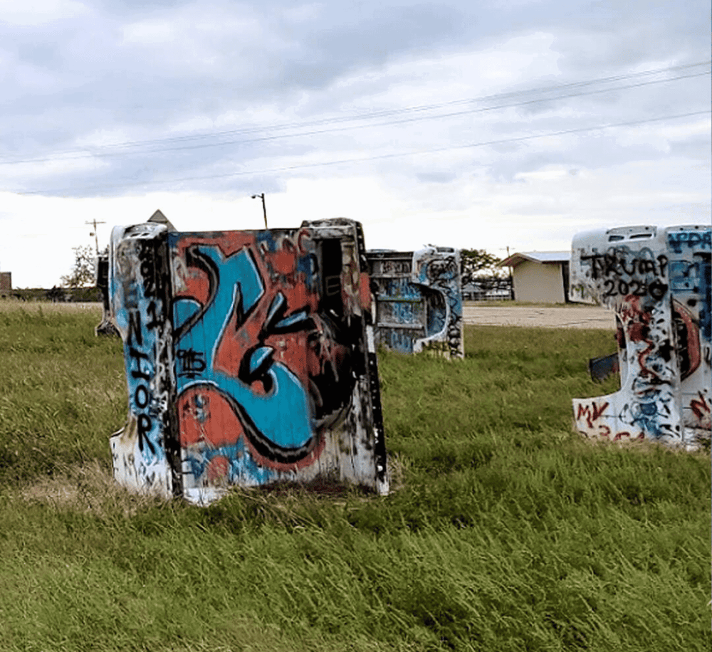 Colorful graffiti on abandoned mailboxes in an open grassy area with a cloudy sky.
