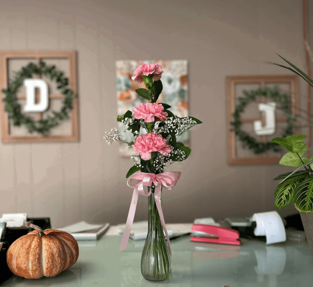Soft pink carnations in a glass vase with a pink ribbon, decorated for a celebration or workplace setting.
